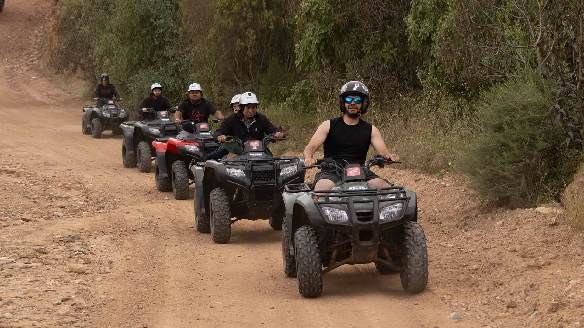A guided group of ATV riders traveling through a wooded dirt trail